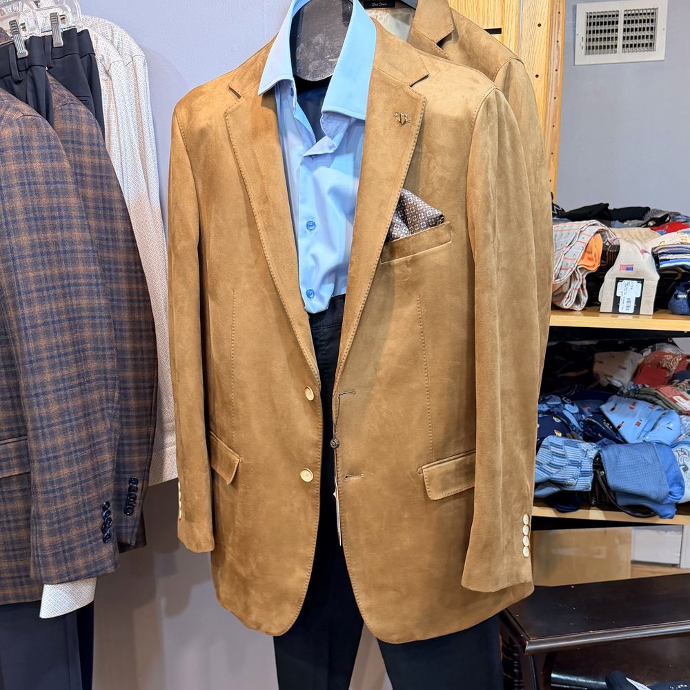 A camel suede sport coat with a blue shirt and pocket square on the men's floor